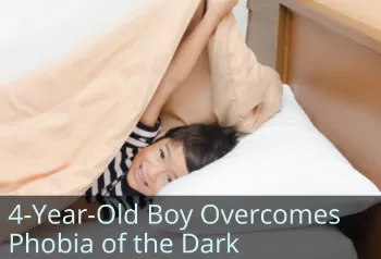 Smiling boy with head on pillow peeking out from under blanket. Text: 4-year-old boy overcomes phobia of the dark.