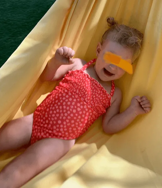 Child in hammock with arms up and hands fisted
