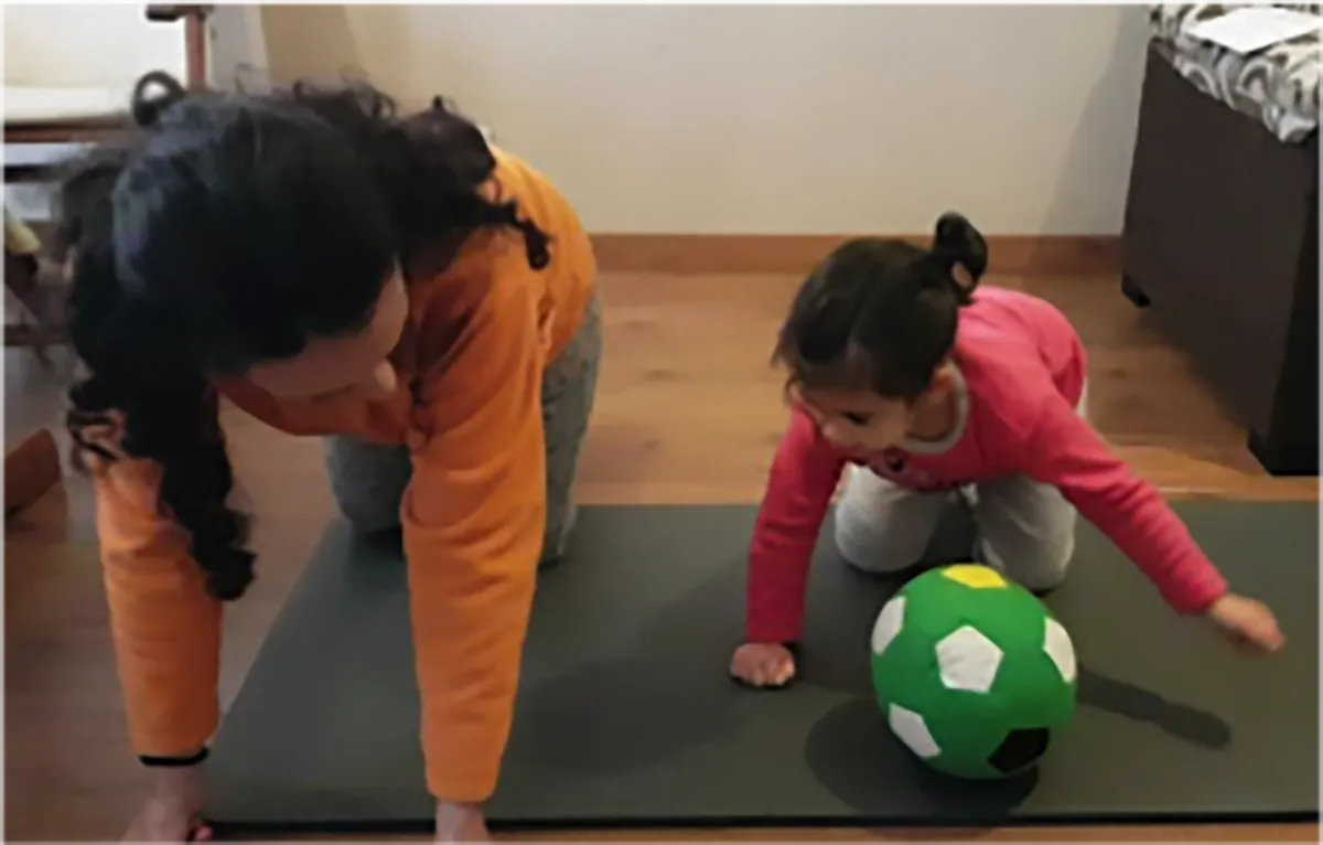 Mother and young daughter in 4-point on the floor passing a green and white soccer ball to each other