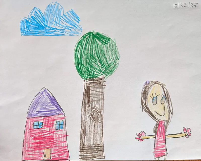 A clearly drawn red house with blue rood, complete with windows. In the middle is a tree with a rectangular colored-in trunk and a green circle above representing the bushy part of the tree. To the right is a person with a head and features, in a red striped dress and her arms sticking out to the side. The crayon colors are dark, indicating confident strokes.