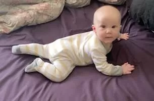 Baby in prone on a bed looking at the camera.