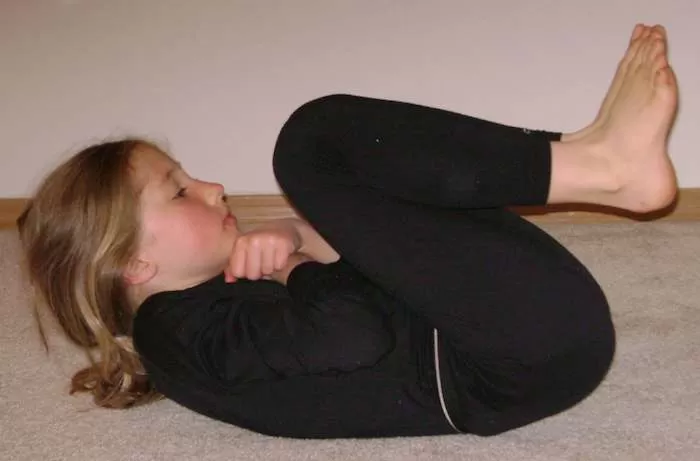 young girl curled up in a ball from supine position, doing neurodevelopmental movements to integrate the Moro reflex