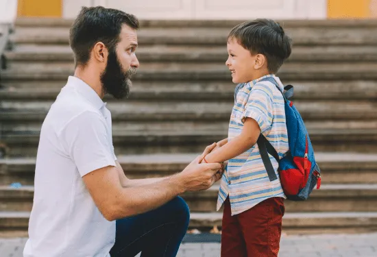 Father and son saying goodbye before school. The father is kneeling at son's level, and there is strong, comfortable eye contact between the two.