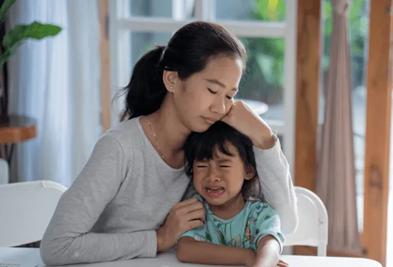 Mother holding crying child sitting at the table