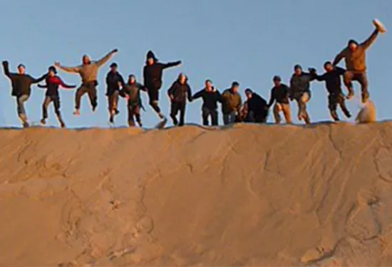 Row of people jumping off the top of a sand dune on a sunny day
